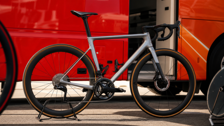 Illustrazione editoriale di un prototipo da salita con foderi sottili nel paddock del Tour de France 2026